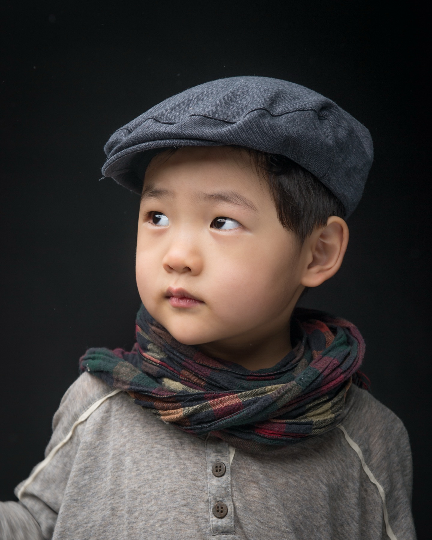 Soohyun Kim's son in a cap and scarf against a dark studio background