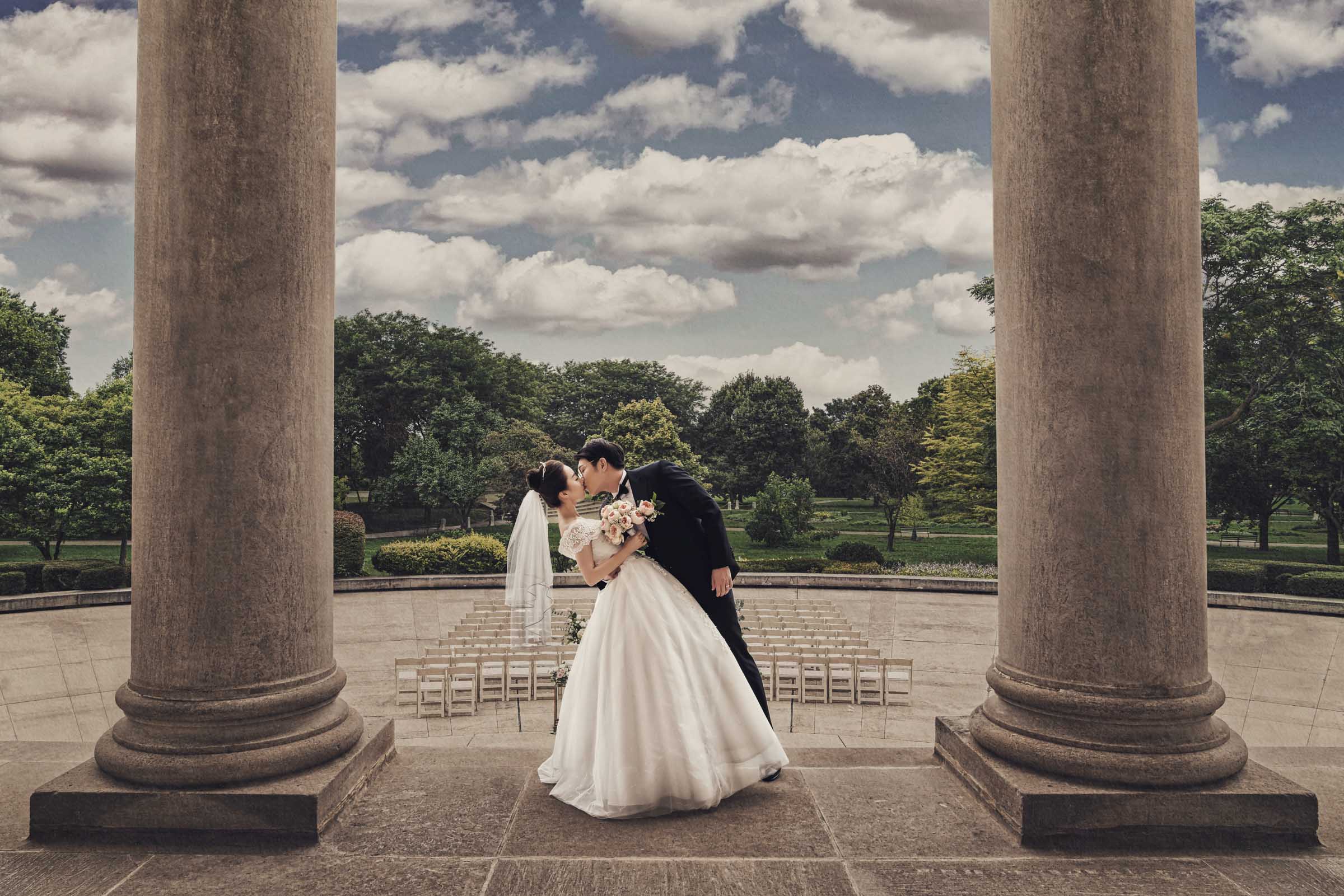 Newlyweds kissing between columns at an outdoor wedding setting