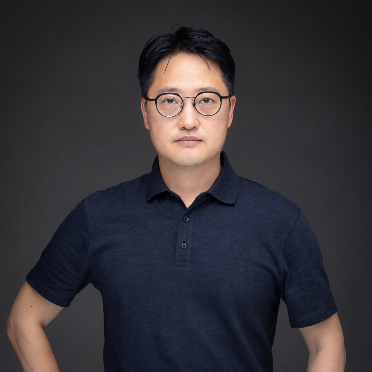 Soohyun Kim wearing glasses and a navy polo against a charcoal background